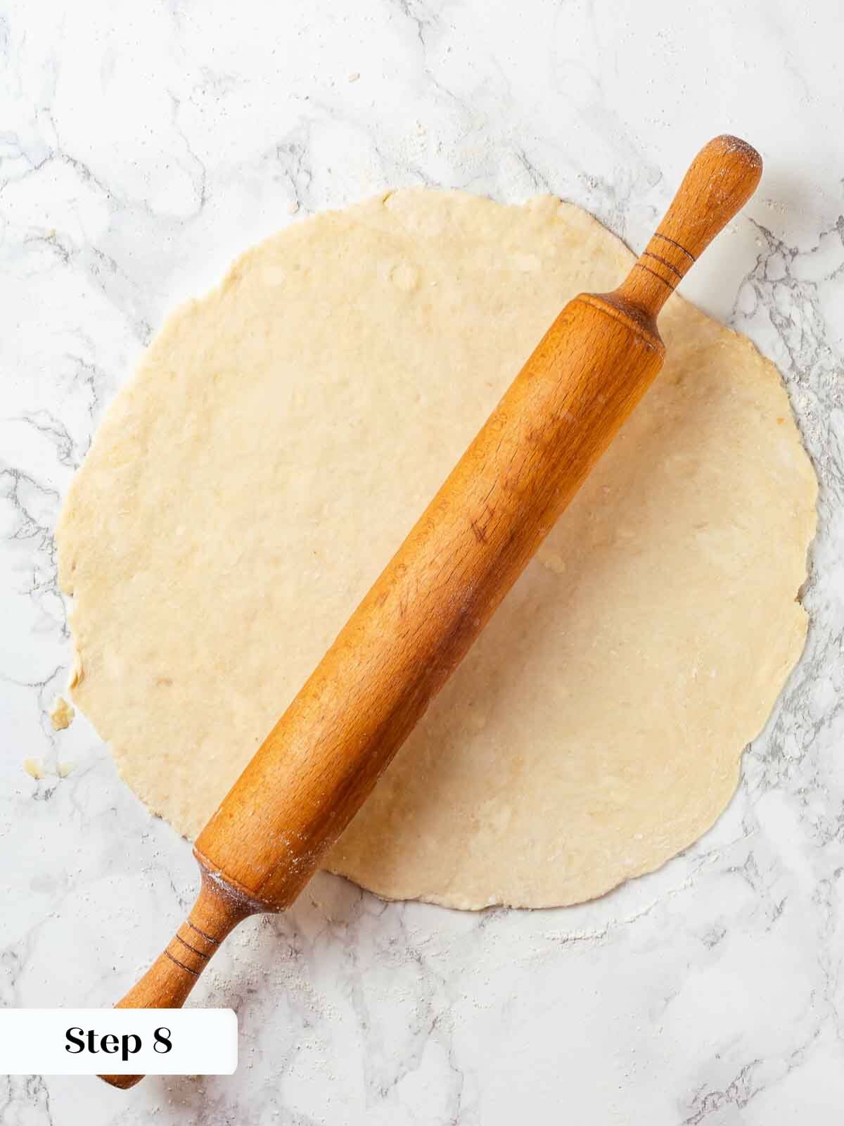 A rolling pin flattening out pie crust dough on a surface.