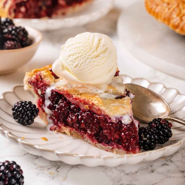 A thick slice of blackberry pie served on a white scalloped plate.