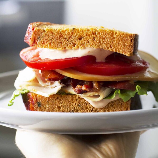 homemade bacon turkey bravo sandwich on white plate in hand.