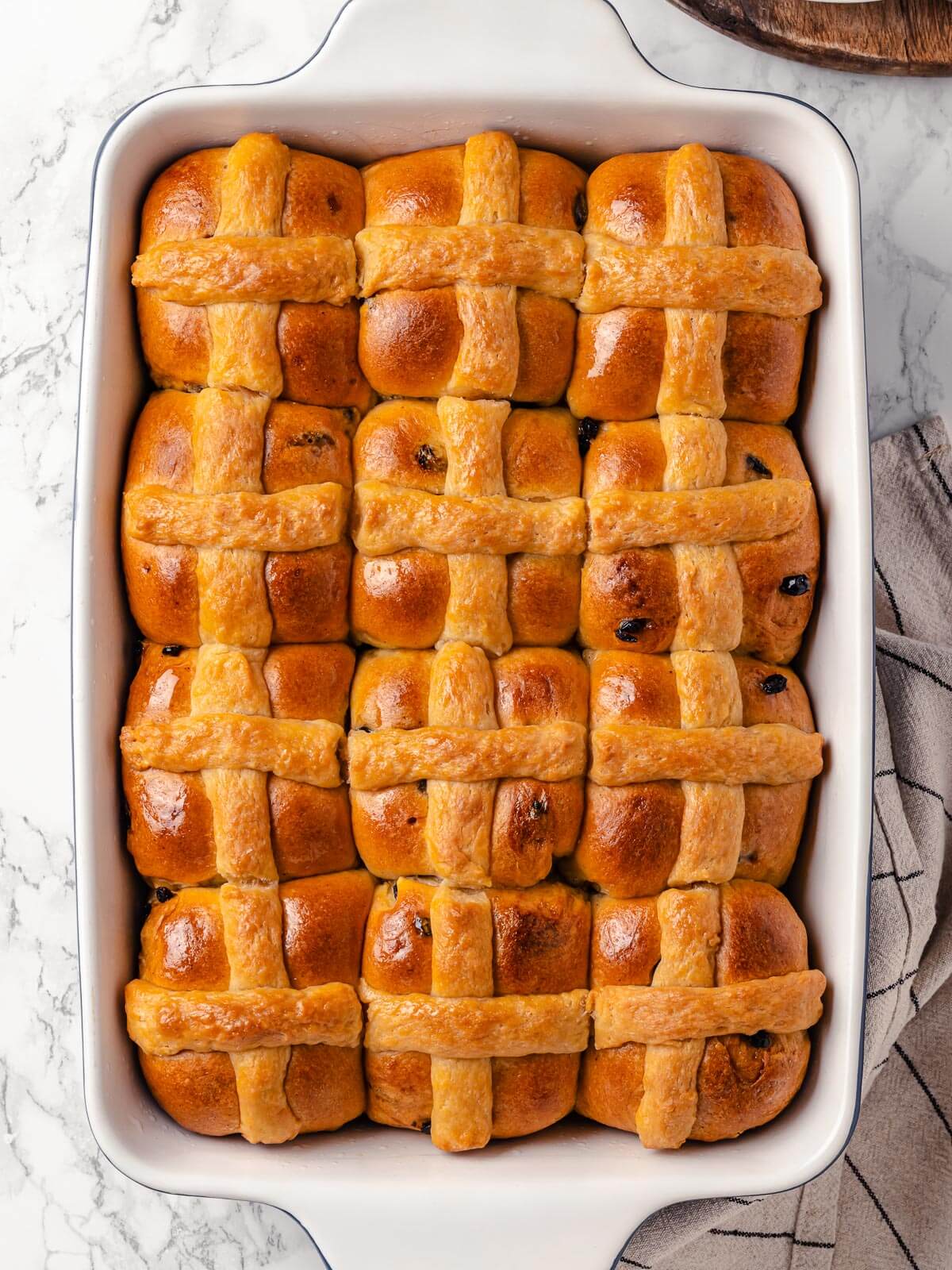 A tray of golden-brown hot cross buns fresh from the oven.