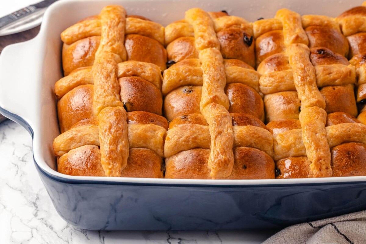Hot cross buns arranged in a blue baking dish.