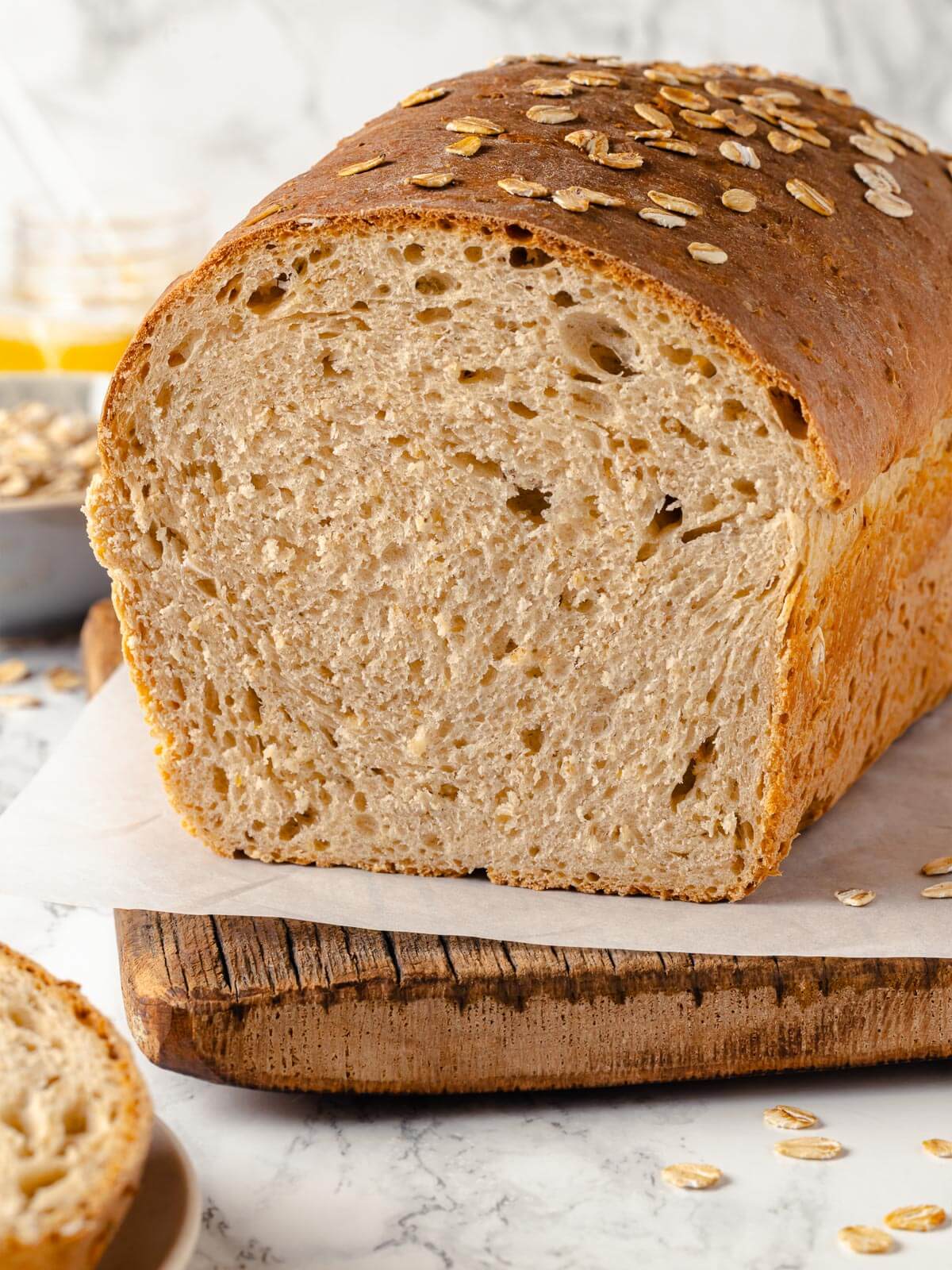 Whole loaf and slices of oatmeal bread on a cutting board.