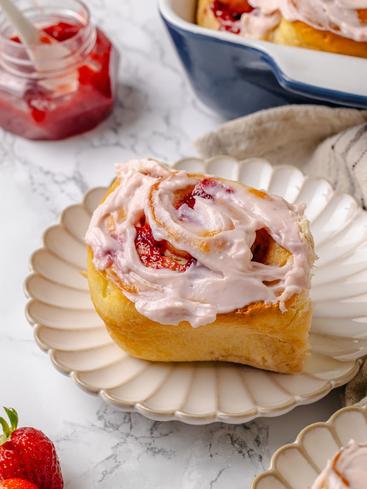 Iced strawberry cinnamon roll served on a white plate.