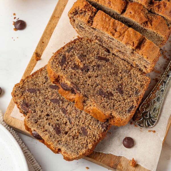 Full loaf of banana bread sliced on parchment-lined surface after cooling.