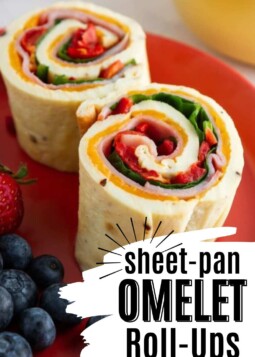 Two sheet-pan omelet roll-ups filled with spinach, red pepper, and ham on a red plate, served with fresh blueberries and a strawberry.
