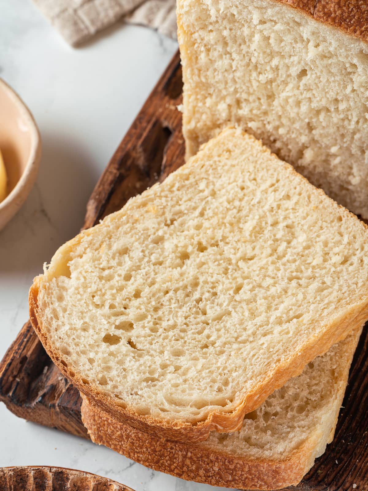 Loaf of sliced golden sourdough sandwich bread displayed on marble counter surface, freshly baked.