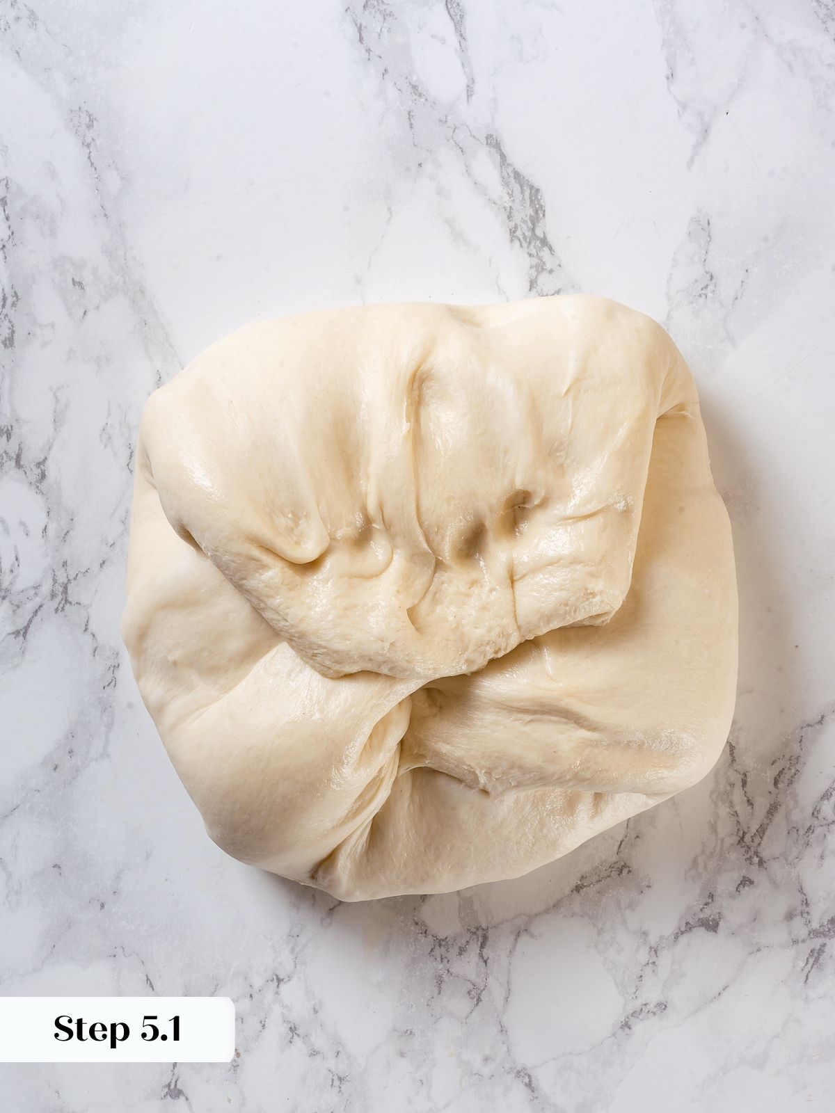Dough being folded over itself during sourdough shaping process, preparing for loaf formation.