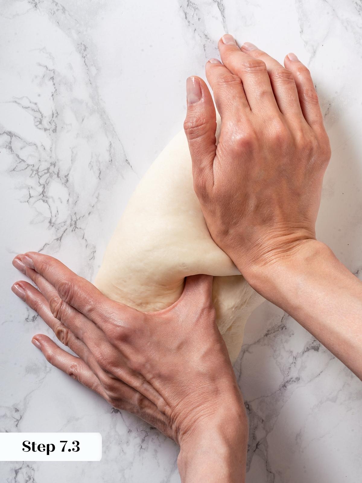 Hand sealing shaped sourdough dough log during bread making, folding and pressing dough edges closed.