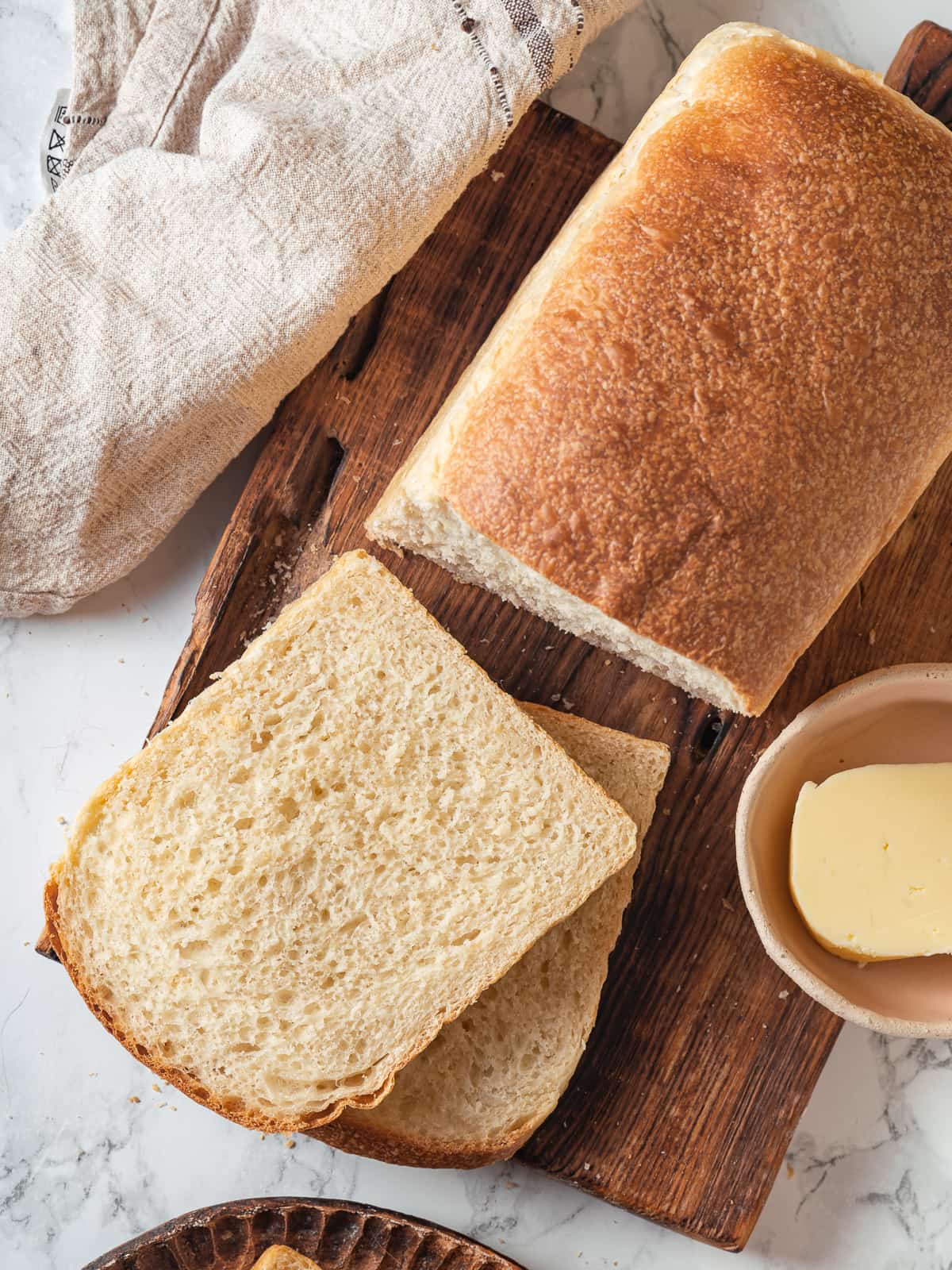 Loaf of sourdough sandwich bread resting on a wooden cutting board, freshly baked and sliced.