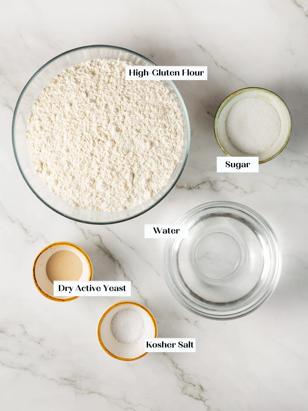Ingredients for homemade bagels arranged on a countertop including flour, yeast, water, sugar, and salt.