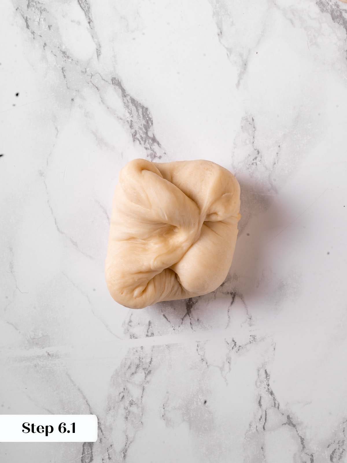 Dough being tucked and shaped into a rounded roll with careful hand movements.