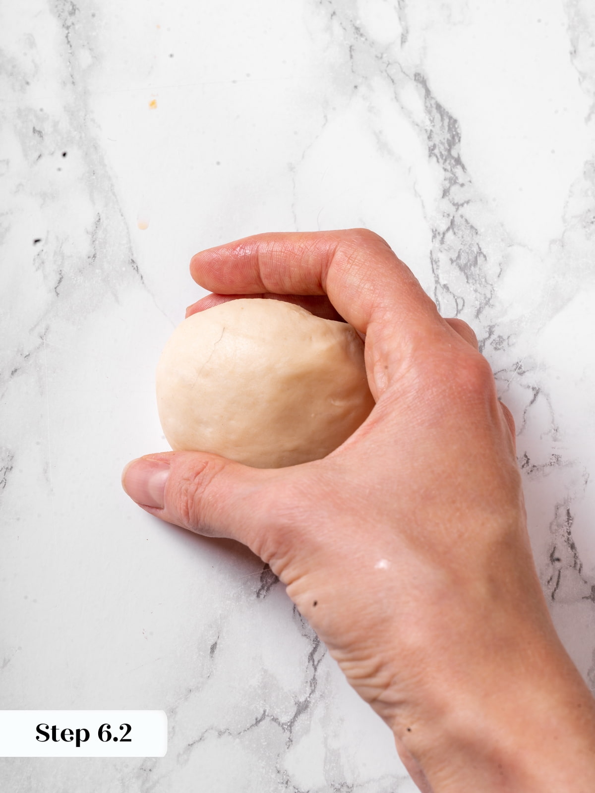 Dough being rolled into a tight ball with hands creating surface tension.
