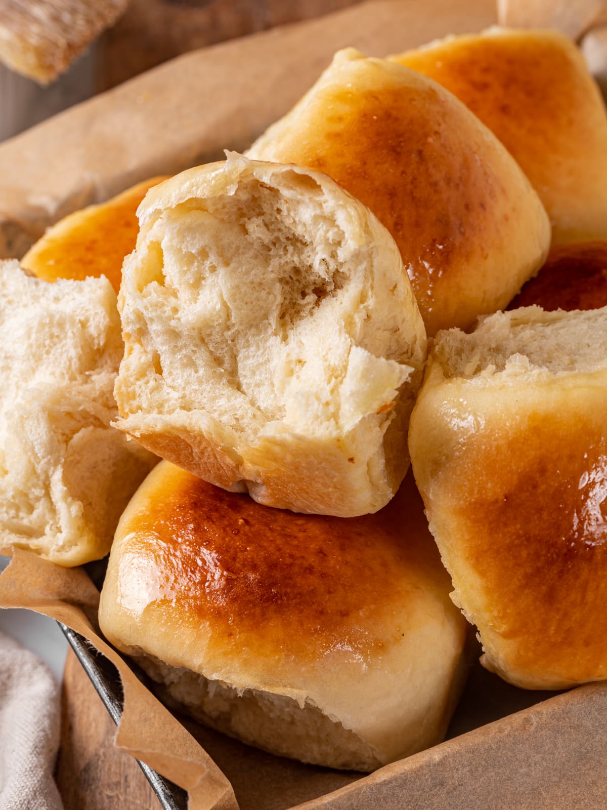 A torn sourdough roll revealing its soft crumb while resting among other warm rolls.