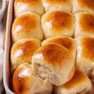 A soft roll resting above several more highlighting its fluffy crumb and warm surface.