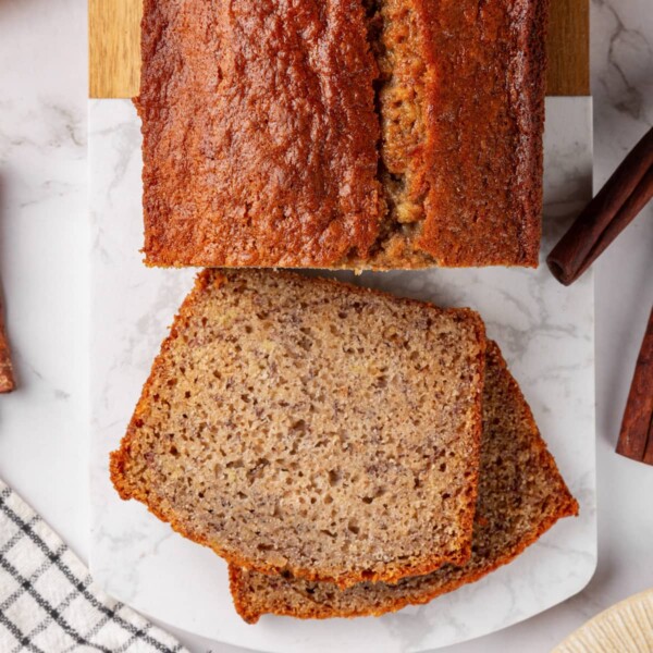 Two slices of sourdough banana bread with full loaf on marble board.