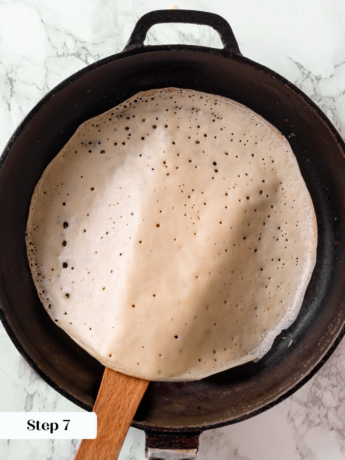 Thin sourdough crêpe mid flip in a skillet during the cooking process.