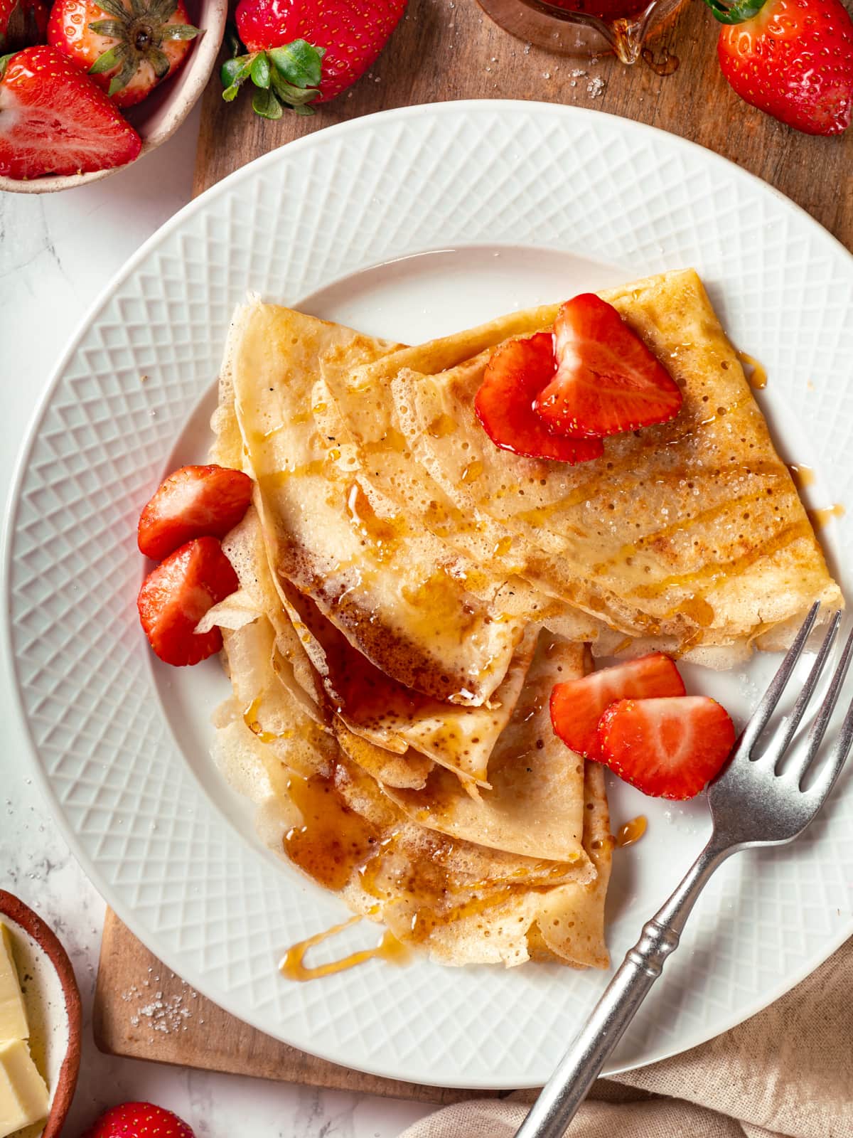 Sourdough crêpe topped with sliced strawberries and maple syrup on a plate.