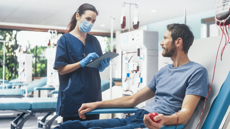 A man giving blood while a female medical professional checks her tablet