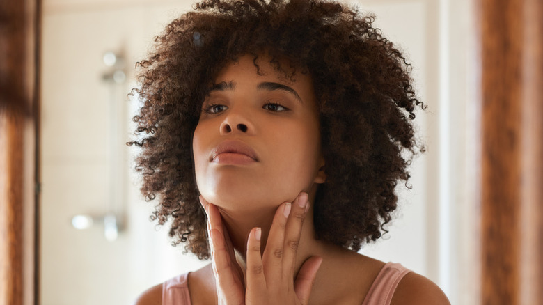 young woman touching her neck while looking in mirror