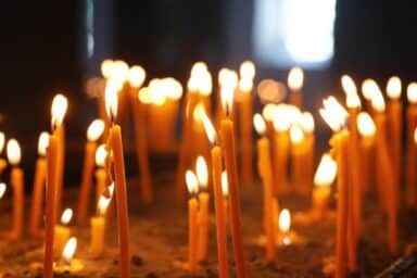 Many thin, lit amber candles glow in a dark room, symbolizing a vigil or memorial service for a loved one.
