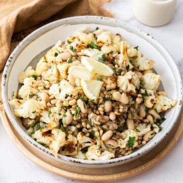 Roasted Cauliflower and White Bean salad on a white plate topped with lemon wedges