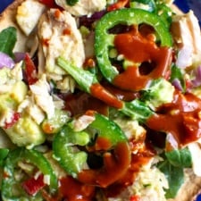 A tostada topped with tuna salad and hot sauce.