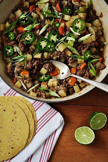 A dish filled with picadillo topped with sliced jalapeños and a lime cut in half.