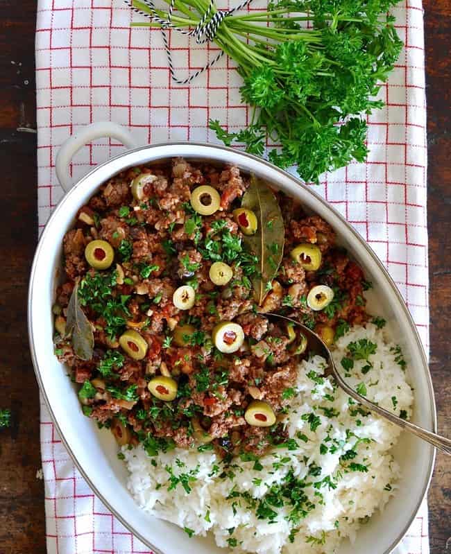 A casserole dish sitting on a red and white tablecloth with a bunch of parsley behind it