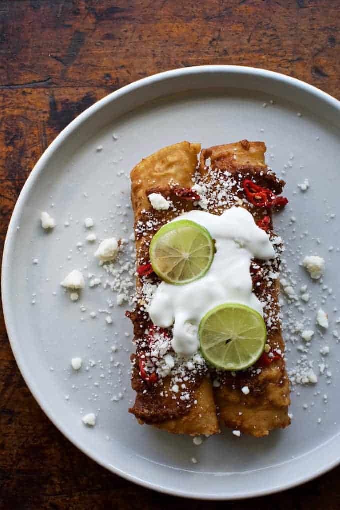 Two enchiladas covered with crema and topped with crumbly cheese and two lime wheels.
