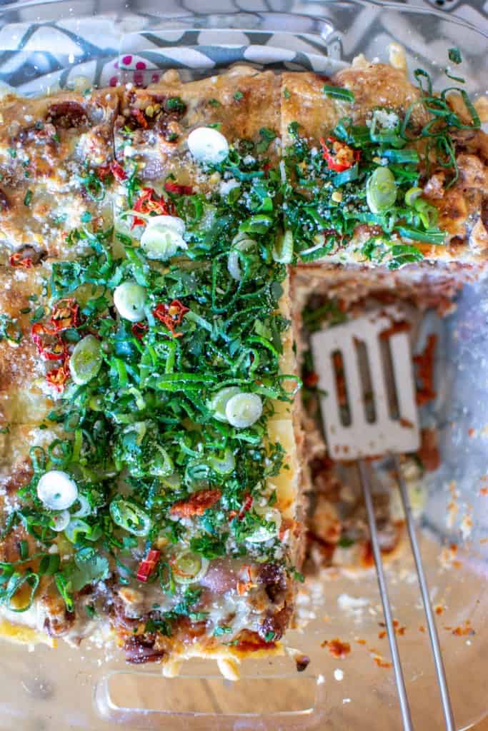 A casserole dish filled with an enchilada casserole with two pieces missing and topped with green onions.