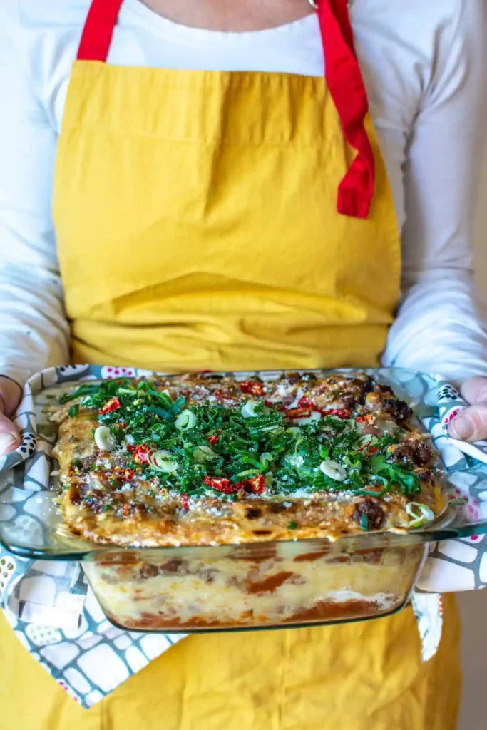A woman wearing a yellow apron holding a casserole.