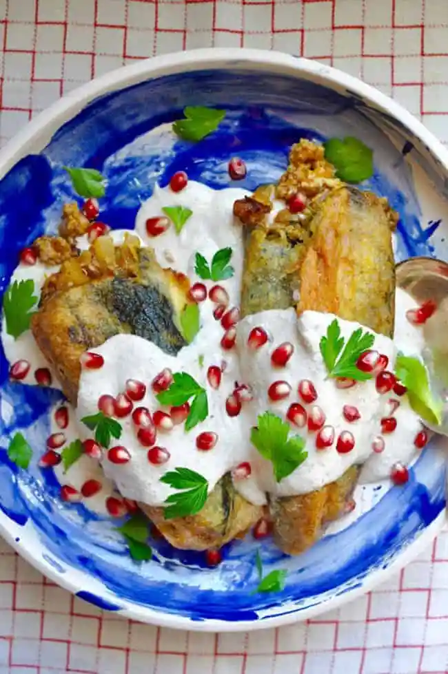 Two poblano peppers stuffed with meat filling and fried and topped with white sauce and pomegranate.