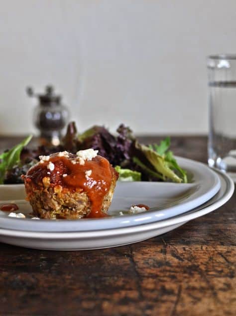A plate with a miniature meatloaf on it and a salad behind it as well as a glass of water.