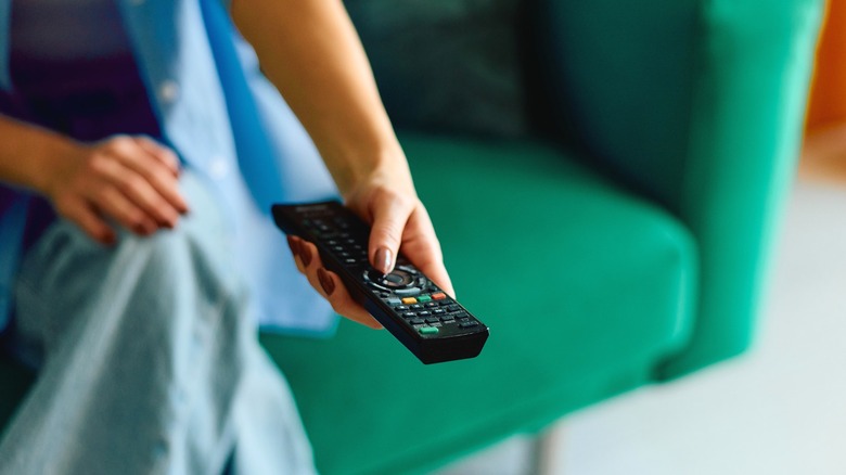 Woman using TV remote while sitting on green sofa