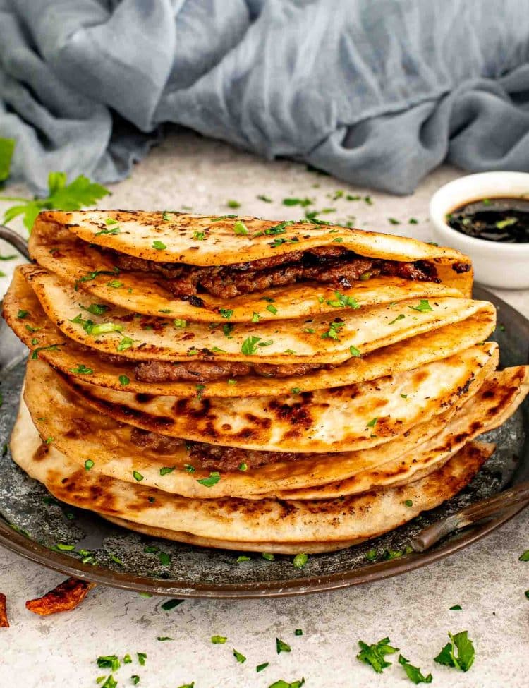 Stack of smashed dumpling tacos cooked until deeply golden and crisp, layered on a skillet with chopped herbs.