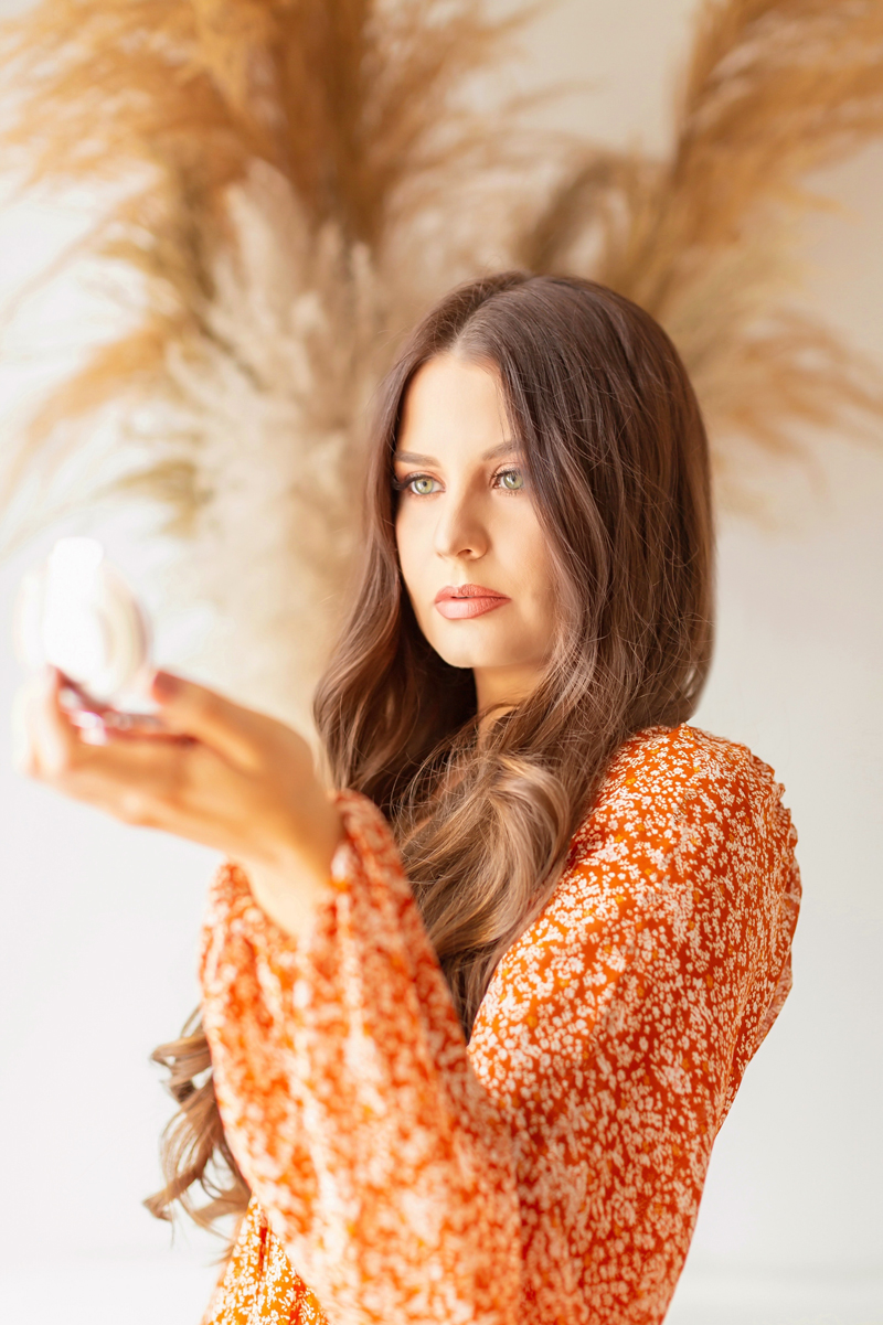 My Top 5 Pumpkin Spice Lipsticks | JustineCelinaβs most worn Physicians Formula Products | Beauty Bloggerβs Favourite Physicians Formula Products | Physicians Formula Organic Wear Tinted Lip Treatment in Gingersnap Photos Review Swatches | The Best Drugstore Fall Lipsticks | The Best Pumpkin Spice Lipsticks for Fall | Fall Lipstick Trends | Brunette woman wearing a burnt orange floral dress holding a compact with pampas grass arrangement in the background | Calgary Beauty Blogger // JustineCelina.com