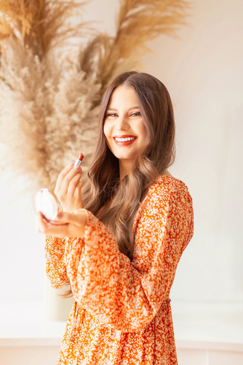 My Top 5 Pumpkin Spice Lipsticks | JustineCelinaβs favourite fall lipsticks | The Best Pumpkin Spice Lipsticks for Fall | Fall 2020 Lipstick Trends | MaybellineΒ Color Sensational Made For All Lipstick in Spice For Me Photos Review Swatches | Light / Medium Skintone | The Best Drugstore Fall Lipsticks | The Best Pumpkin Spice Lipsticks for Fall | Smiling brunette woman wearing an orange floral dress holding a lipstick with a pampas grass arrangement | Calgary Beauty Blogger // JustineCelina.com