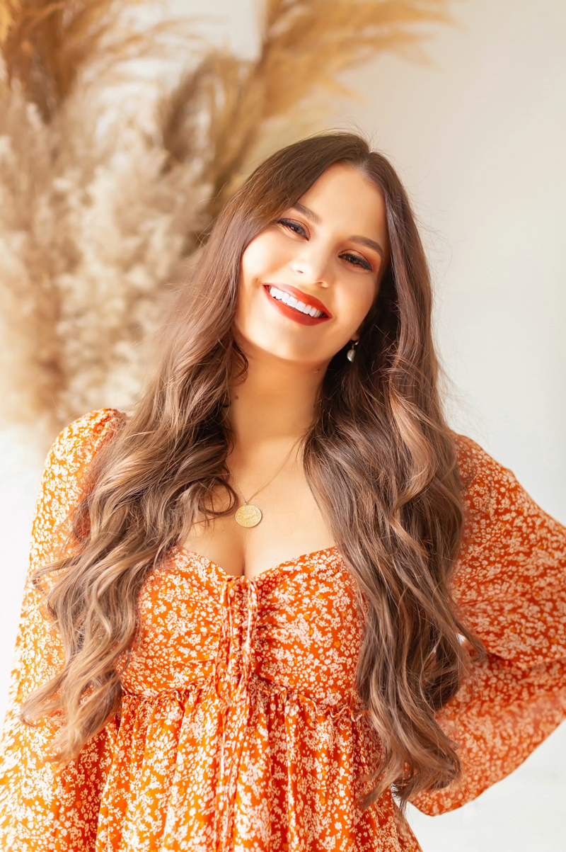 My Top 5 Pumpkin Spice Lipsticks | JustineCelinaβs favourite fall lipsticks | The Best Pumpkin Spice Lipsticks for Fall | Fall 2020 Lipstick Trends | MaybellineΒ Color Sensational Made For All Lipstick in Spice For Me Photos Review Swatches | Light Medium Skintone | The Best Drugstore Fall Lipsticks | The Best Pumpkin Spice Lipsticks for Fall | Smiling brunette woman wearing an orange floral dress and a fall lipstick with a pampas grass arrangement | Calgary Beauty Blogger // JustineCelina.com