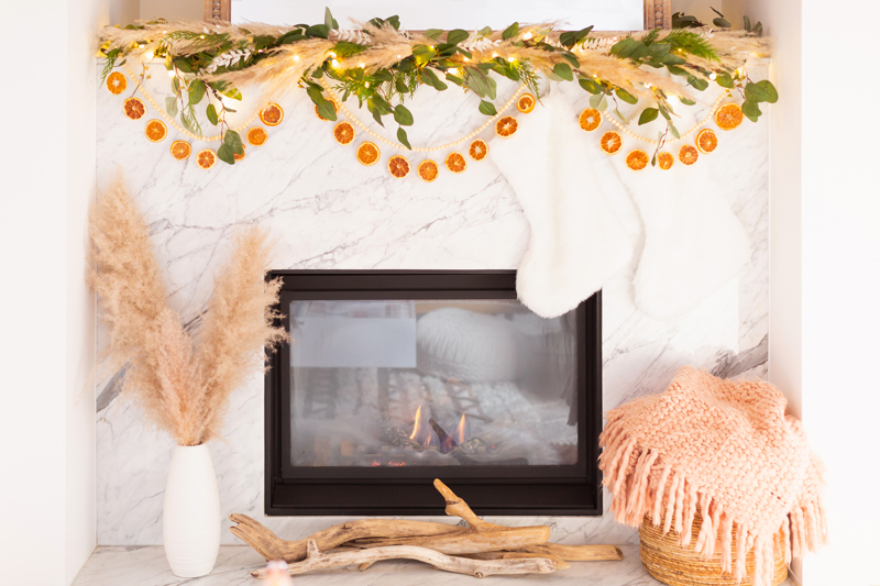 Mid Century Meets Boho Holiday Decor | Bright airy Mid Century Modern Living Room with a boho eucalyptus garland with pampas grass, fresh cedar, bleached Italian ruscus and a beaded dried orange garland | Boho Christmas Decorating Ideas for Apartments | Boho Holiday Fireplace Decor | DIY Orange Slice Garland | Bohemian Holiday Home Tour 2020 | Boho Chic Christmas Decor | Glam neutral holiday decor | Warm toned Holiday decor | Fun Holiday Decor | Dried Fruit Holiday Decor // JustineCelina.com