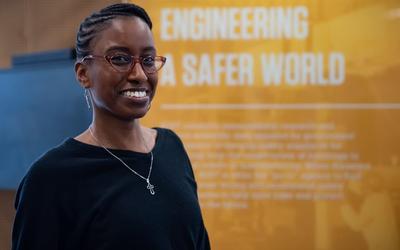 Jazalyn Dukes poses in front of a display that reads "Engineering a Safer World."