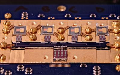 Circuit board with various square chips and gold screws. Small letters in the center say: NIST True Bq.