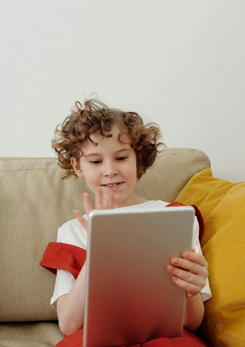 Tween girl waving to someone while holding a tablet.
