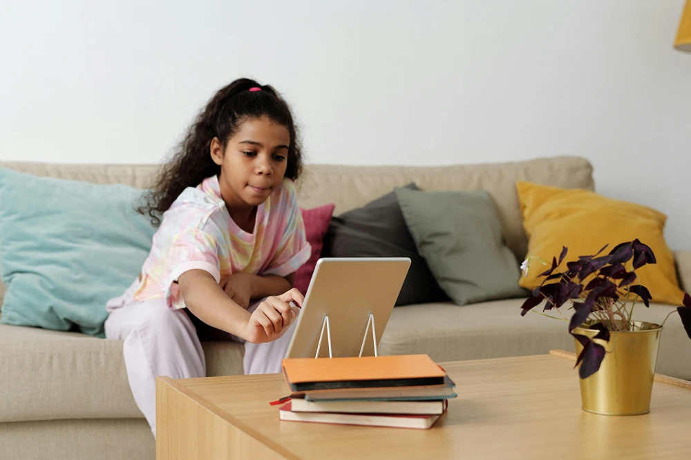 Young teen girl sits on sofa in front of a tablet on the coffee table.