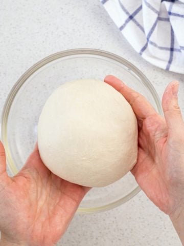 The pizza dough is removed from the stand mixture and is formed into a round ball.