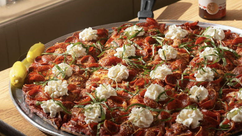 A pizza cut into tavern style squares on a pan with pepperoni, ricotta dollops and basil