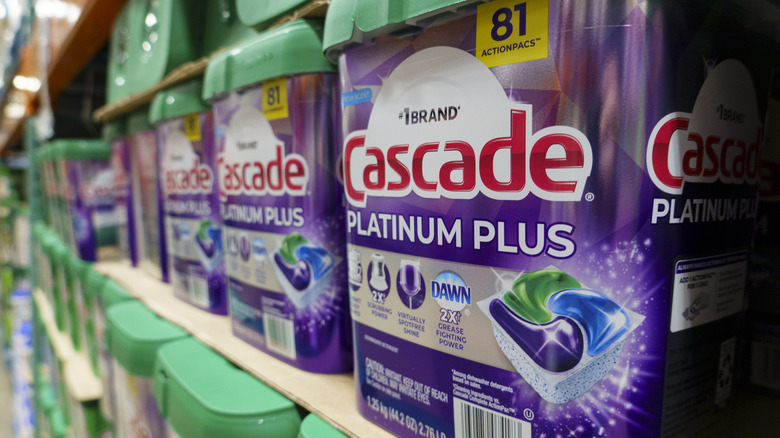 A row of containers of Cascade Platinum Plus dishwasher pod purple and green packages on a shelf in a store