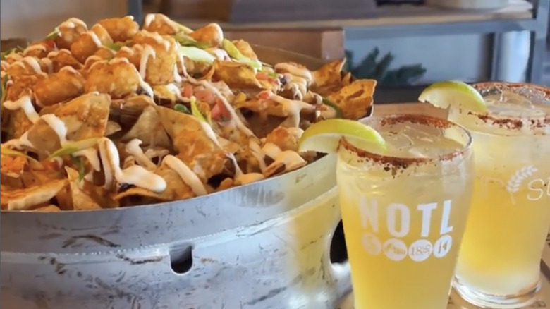 bucket of nachos with sides of sour cream, salsa, extra cheese with two drinks