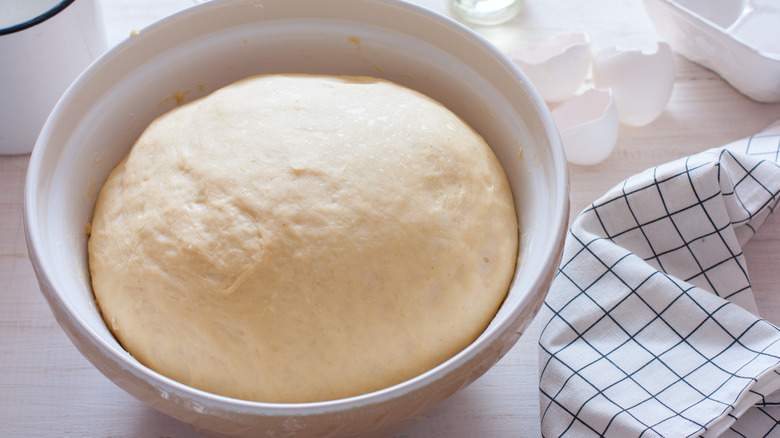 A bowl of bread dough proofing with a towel and egg shells