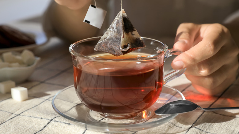 a pyramid tea bag lifting out of a glass cup of tea
