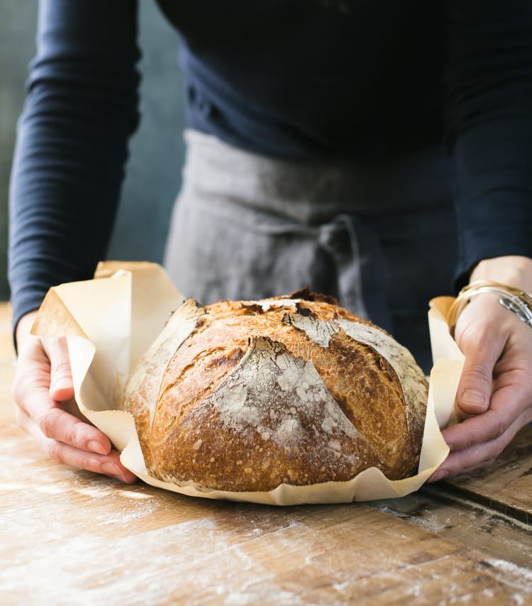 Freshly baked, golden sourdough bread on a parchment lined wood cutting board.